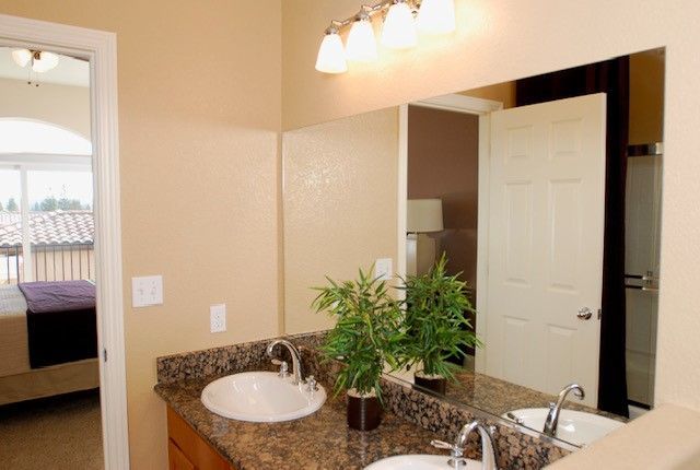 Bathroom with double sinks, large mirror, and open door to a bedroom and a shower.