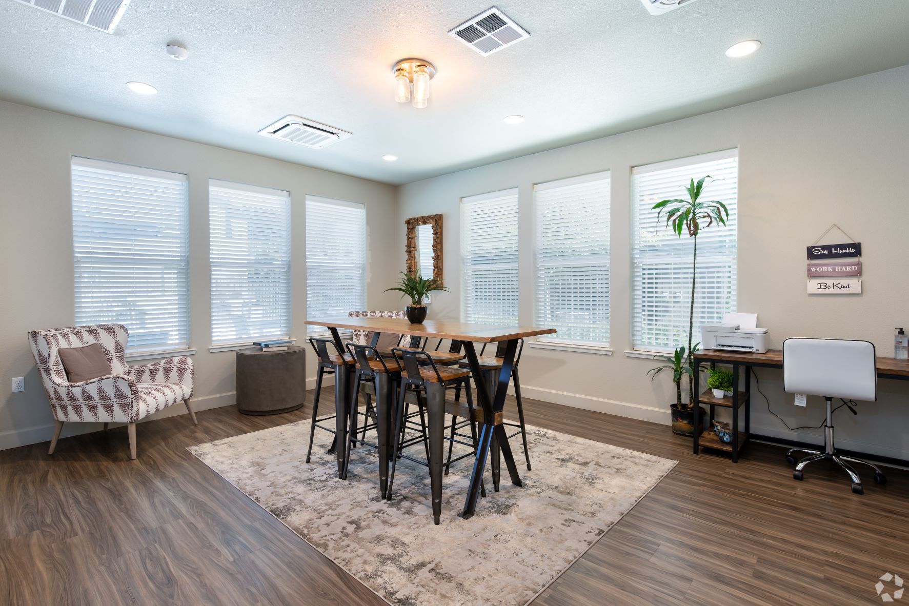 Bright room with windows, a table with stools, armchair, and a desk.