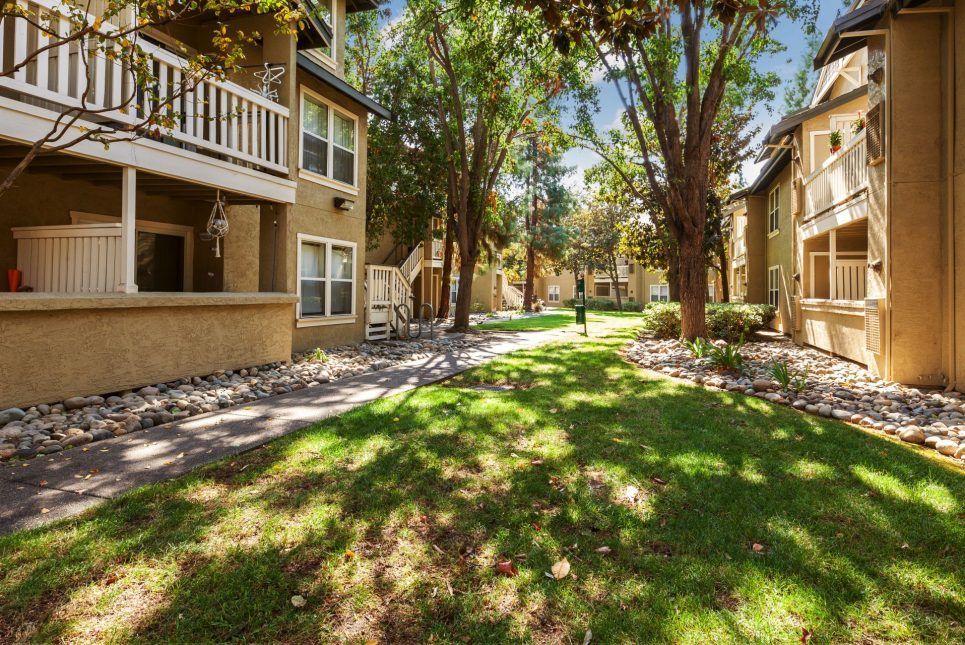 Apartment complex with a grassy path lined with trees and buildings.