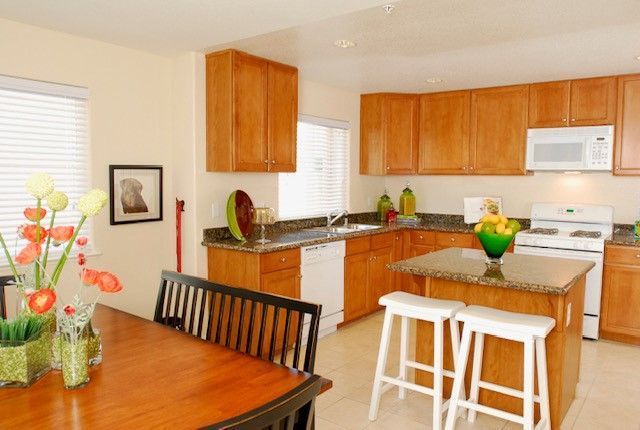 Kitchen with wooden cabinets, white appliances, and a granite countertop island with two stools.