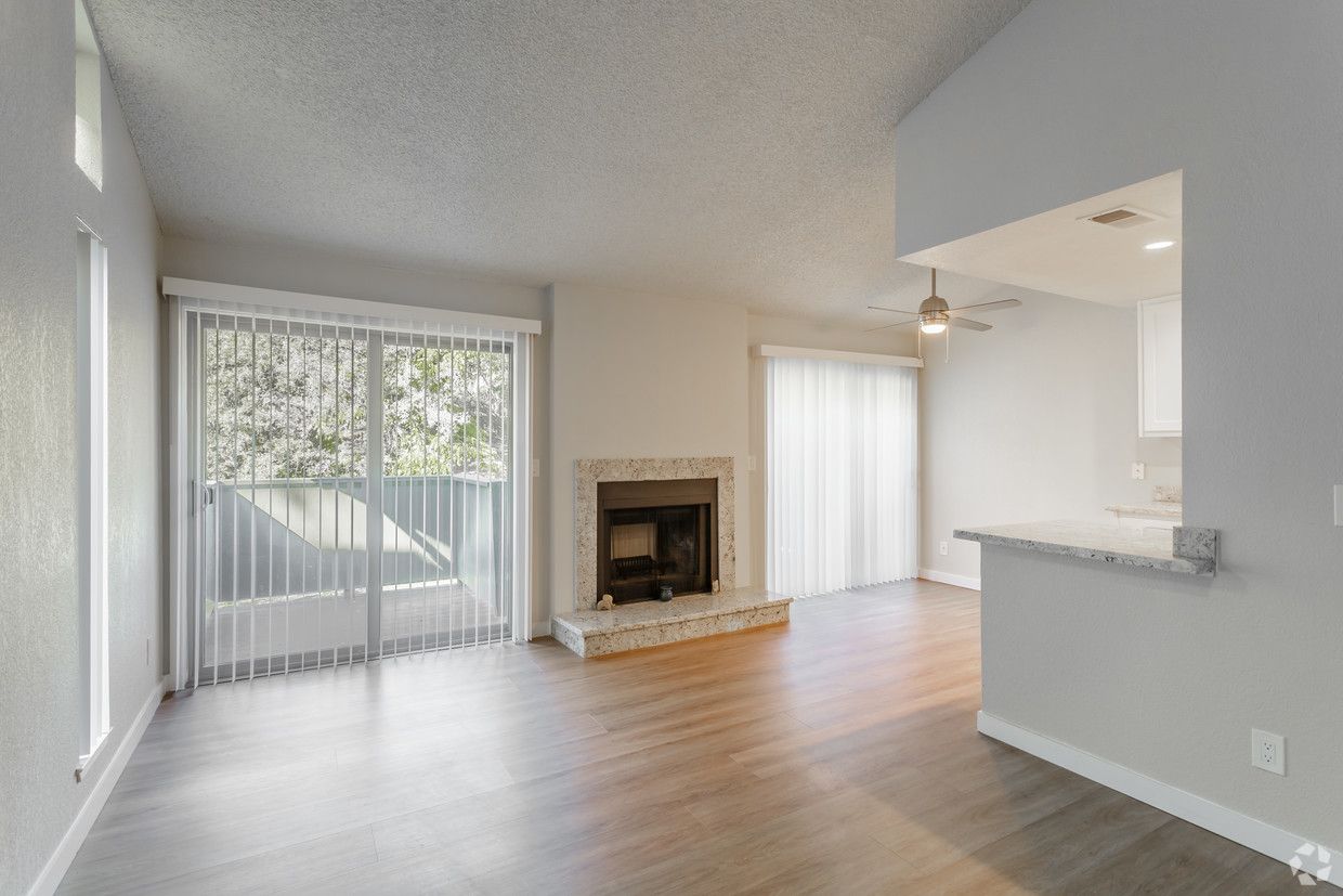 Living room with fireplace, sliding glass door, and wood floors. Neutral tones, well-lit.