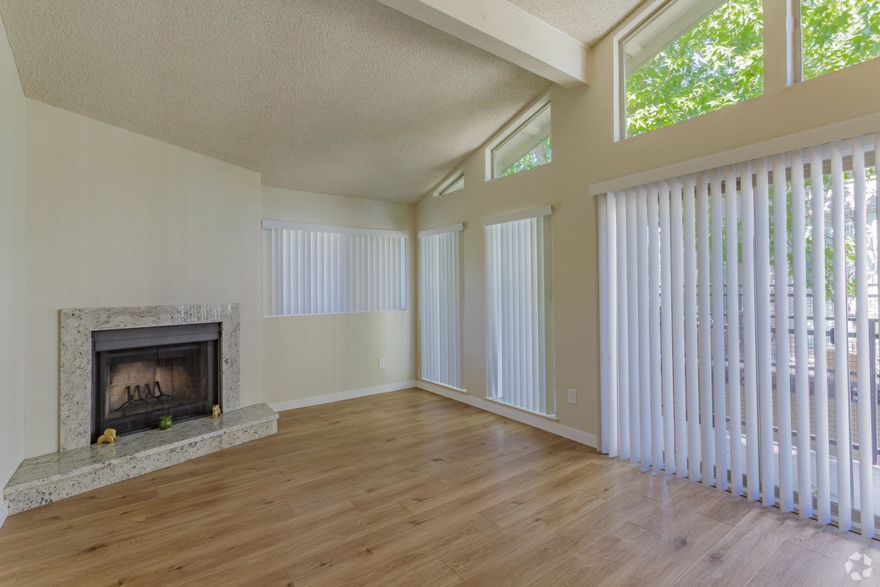 Empty living room with fireplace, wood floor, and large windows.