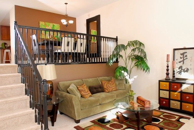 Living room with loft dining area; beige and brown walls, green sofa, patterned rug.
