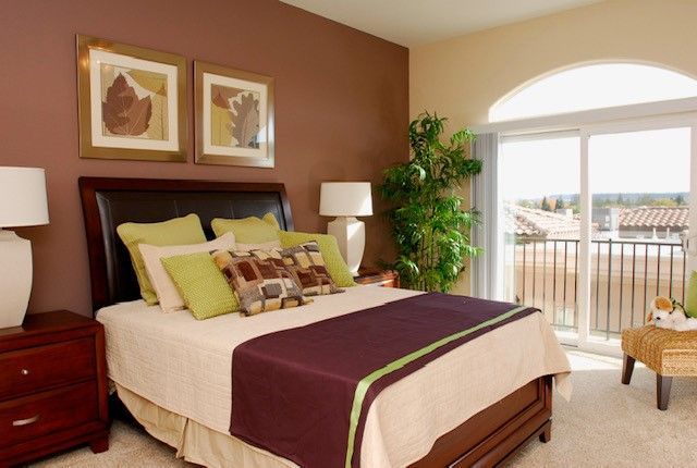 Bedroom with brown walls, bed with purple and green accents, and sliding glass door to balcony.