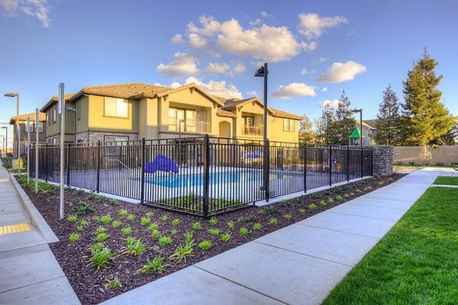 A community pool area with a fence, landscaping, and a two-story building in the background under a blue sky.