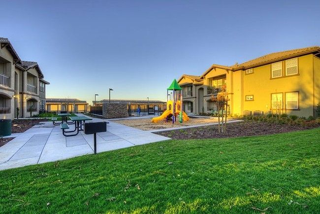 Playground and picnic area in front of multi-unit residential buildings on a sunny day.