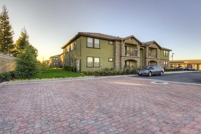 Apartment building with stone accents, brick parking lot, and parked car.