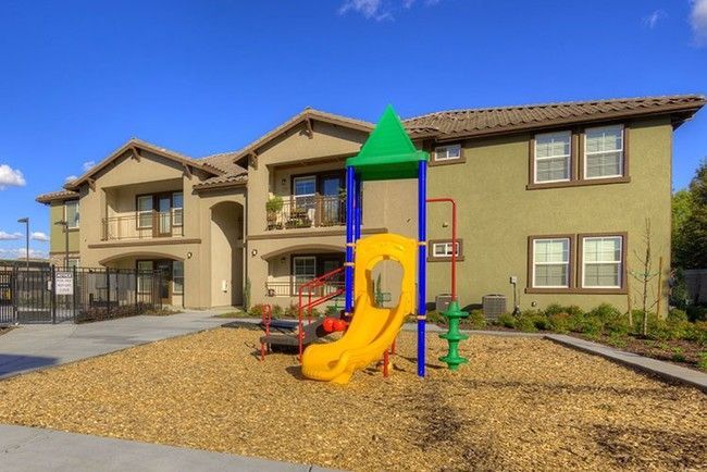 Playground with slide in front of apartment building, gravel ground, sunny day.