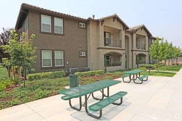 Two-story apartment building with green picnic tables on a sidewalk.