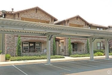 Apartment building with covered parking. Exterior has brick facade, brown roof, and parking spaces.