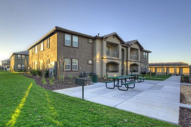 Apartment building with green picnic tables and walkway on a sunny day.