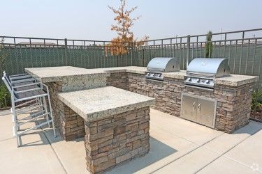 Outdoor kitchen with two grills, stone facade, and concrete countertops.