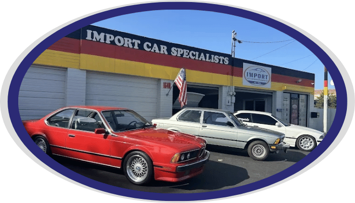 A row of three vintage BMW cars parked in front of Import Car Specialists with German flag colors on the exterior wall.