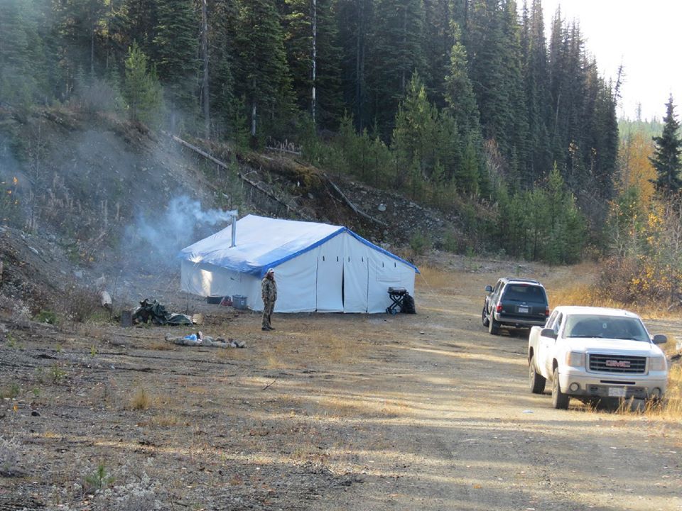 A white truck is parked in front of a tent in the middle of a dirt road.