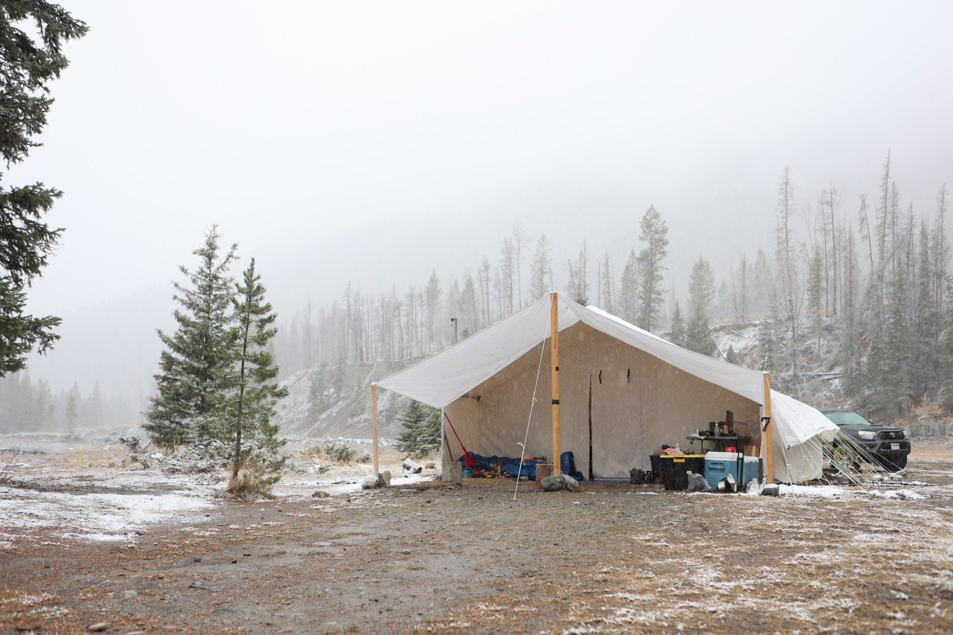 A tent in the middle of a snowy field with trees in the background