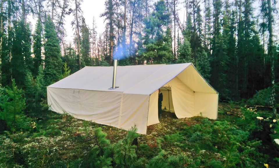 A tent in the middle of a forest with smoke coming out of it