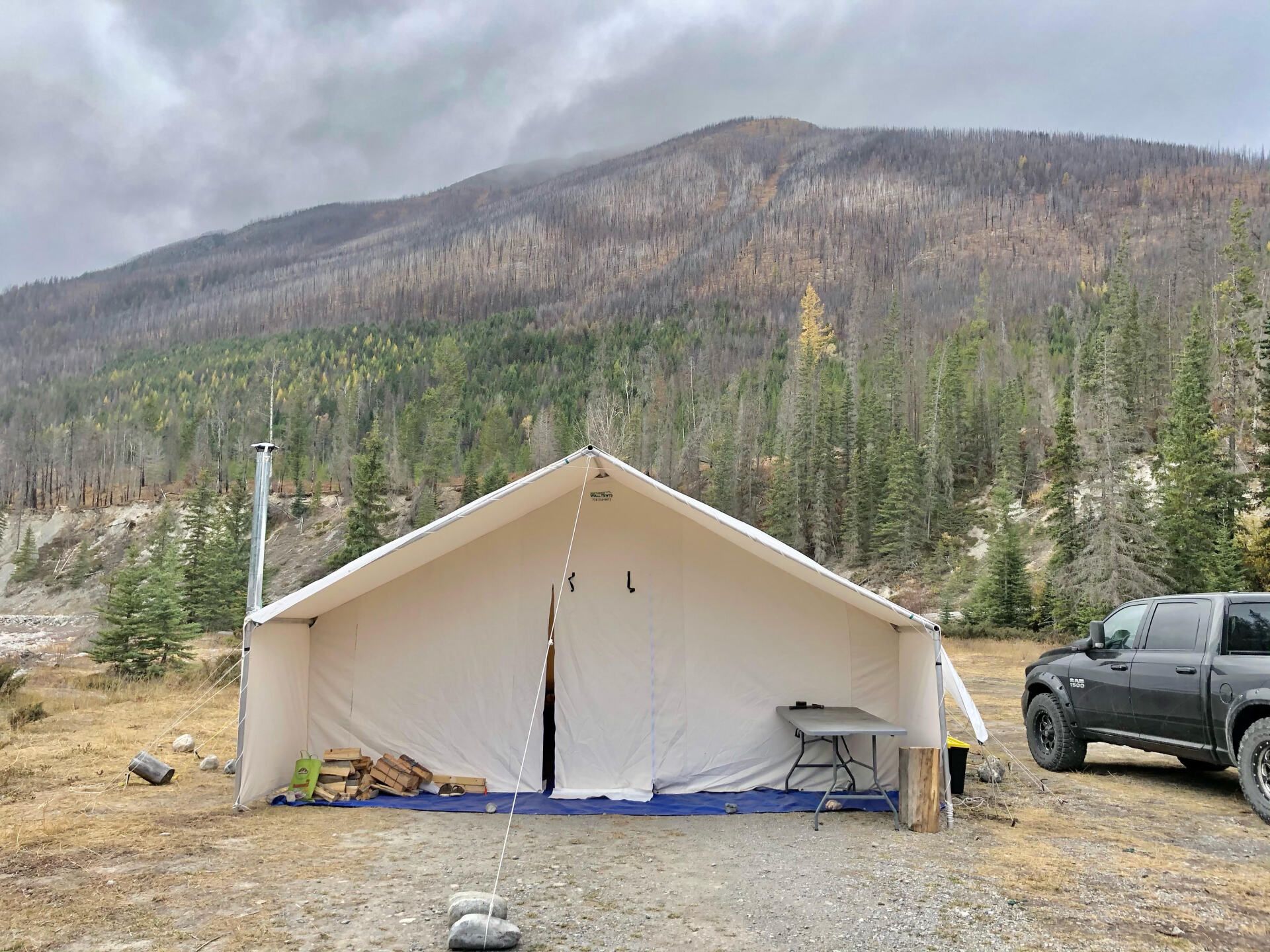 A truck is parked in front of a tent in the woods.