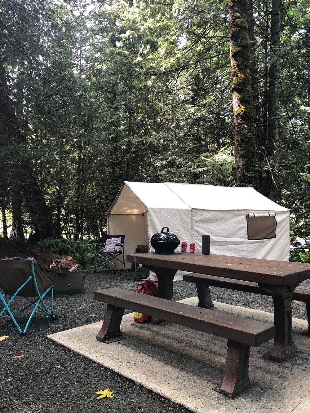 A picnic table in front of a tent in the woods.