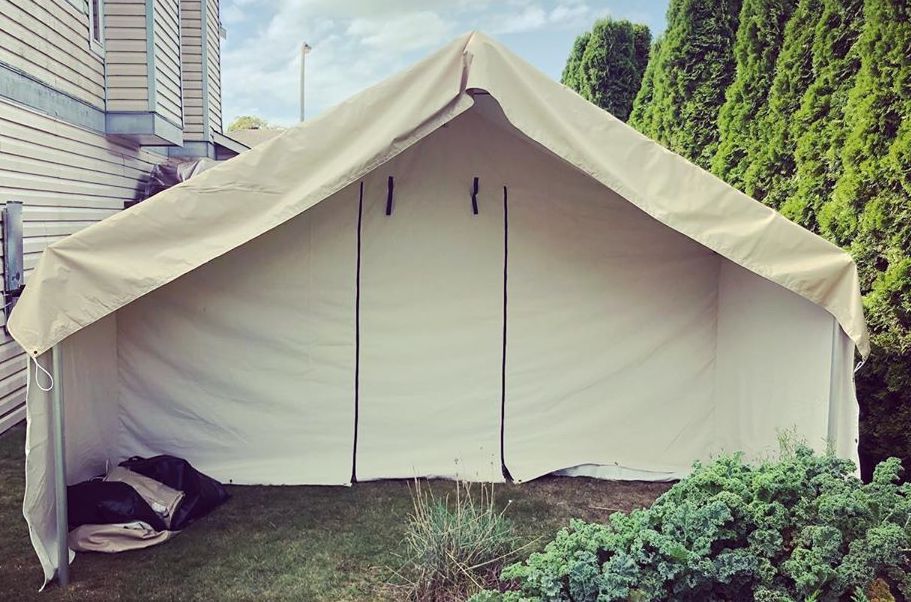 A large white tent is sitting in the grass in front of a house.