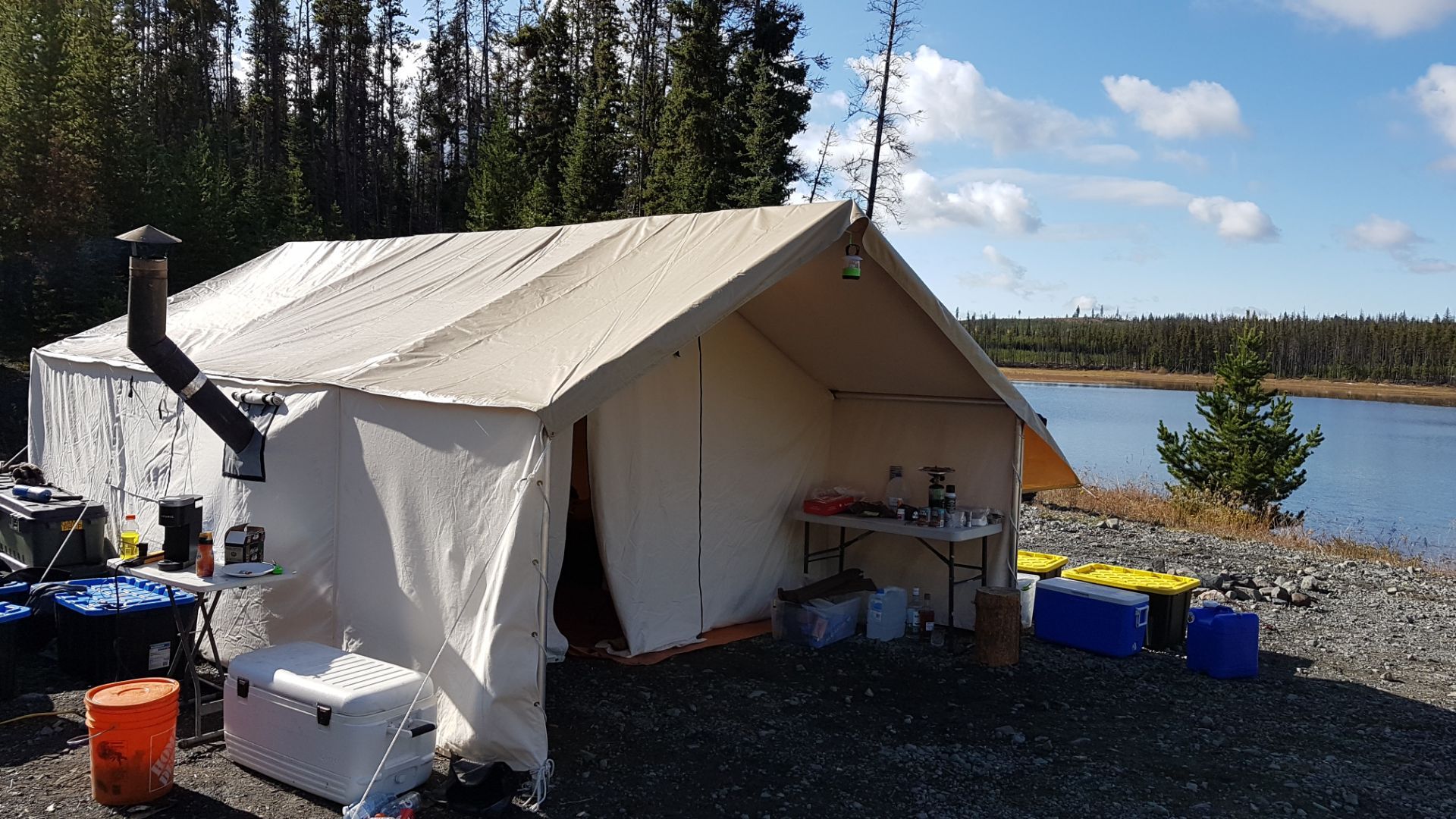 A white tent with a chimney is sitting next to a lake