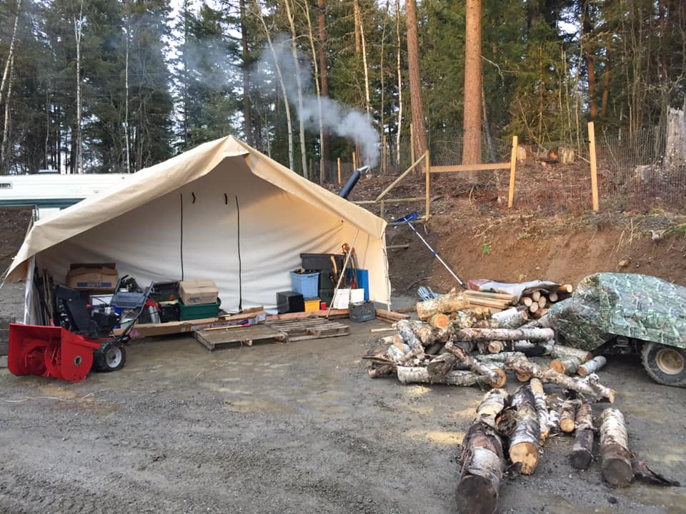 A snow blower is parked in front of a tent in the woods