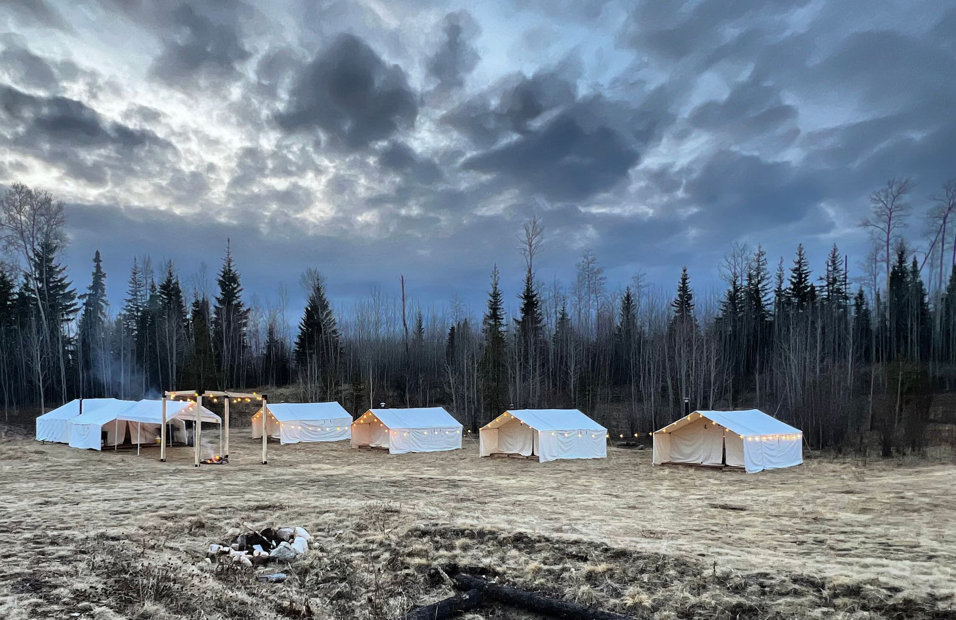 A row of tents in a field with a cloudy sky in the background.
