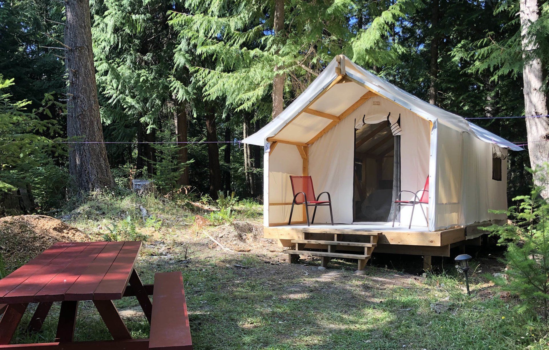 A tent is sitting in the middle of a forest next to a picnic table.