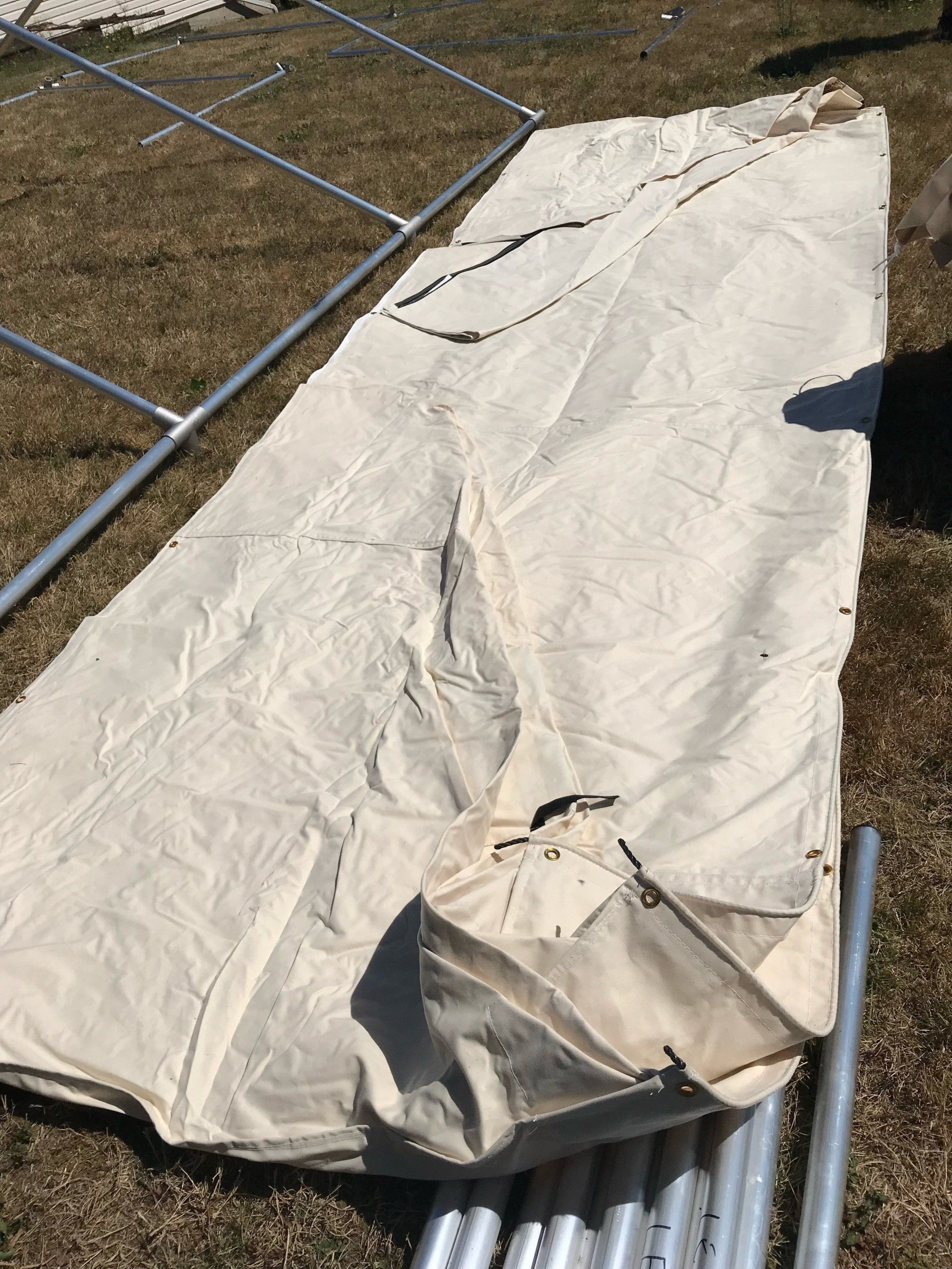 A white tarp is laying on the ground next to metal poles.