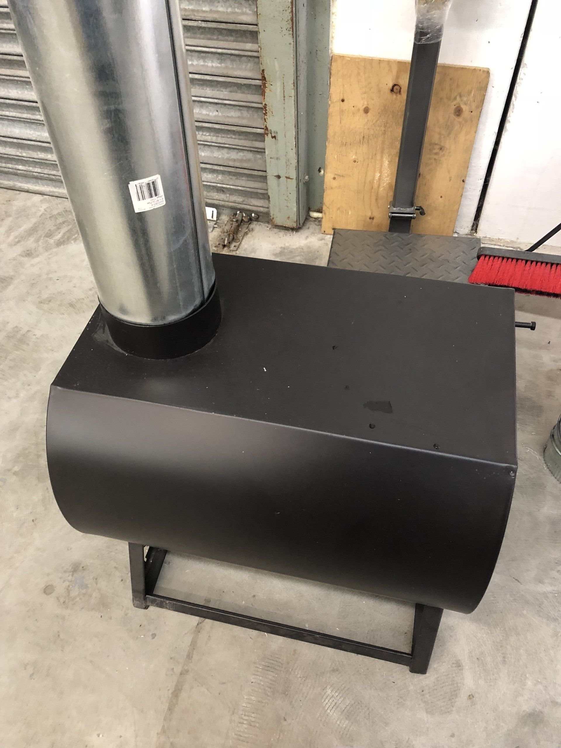 A black stove with a metal pipe coming out of it is sitting on a concrete floor.