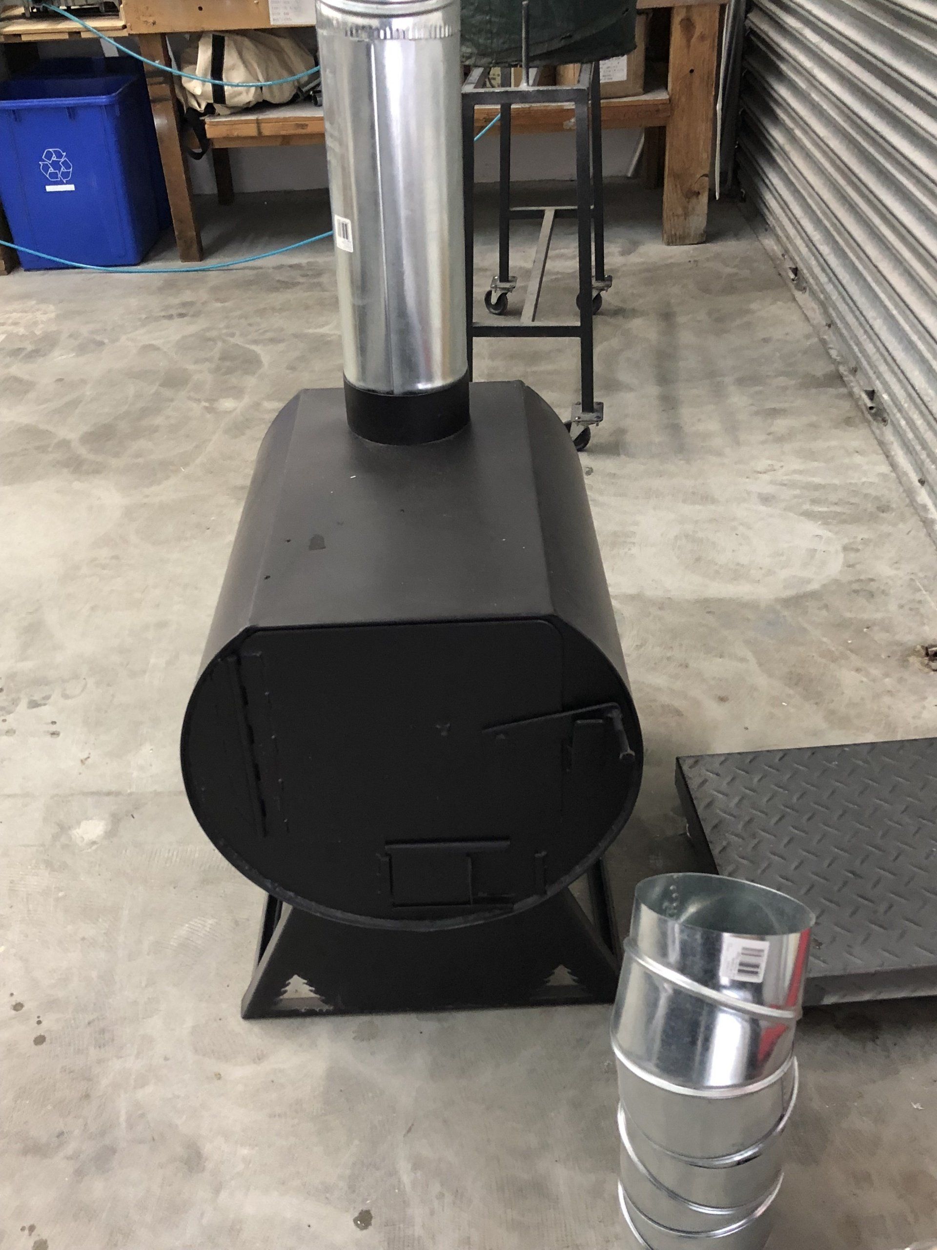 A black stove is sitting on a concrete floor next to a metal pipe.
