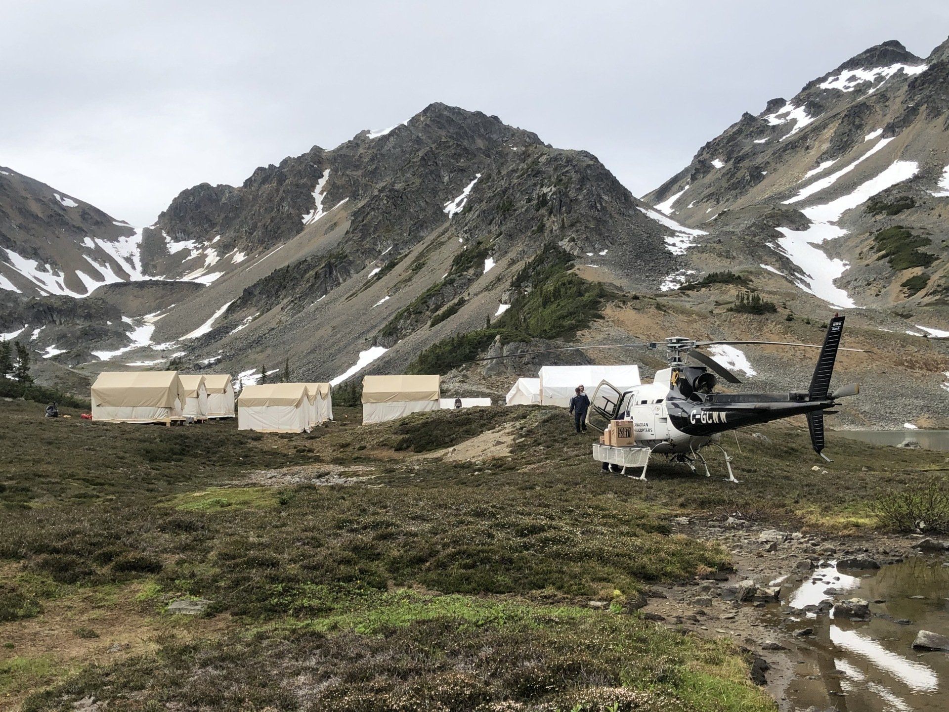 A helicopter is sitting in the middle of a field in front of a mountain.