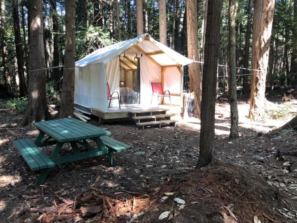 A tent is sitting in the middle of a forest next to a picnic table.