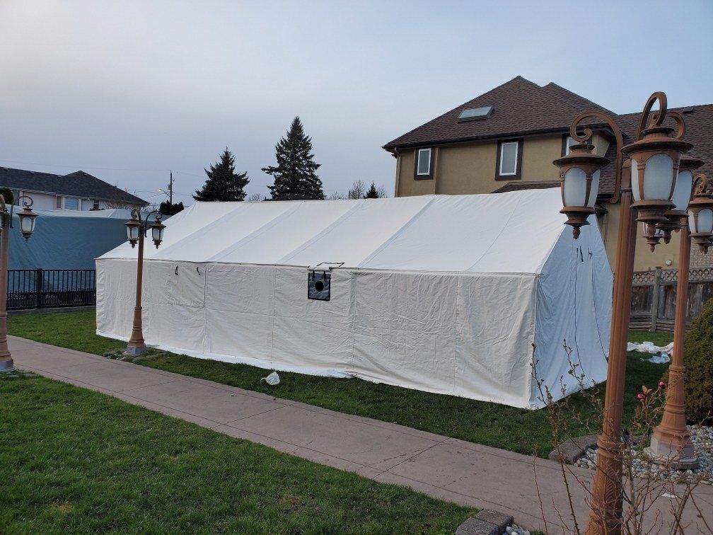 A large white tent is sitting in the grass in front of a house