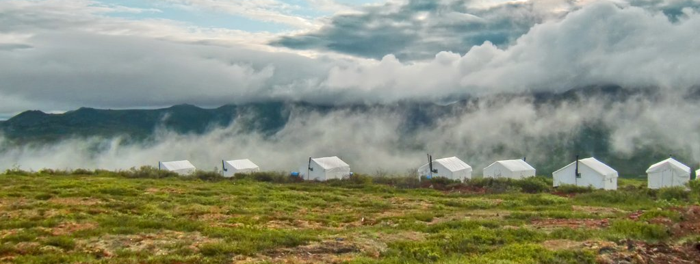 A row of tents in a field with mountains in the background covered in clouds.