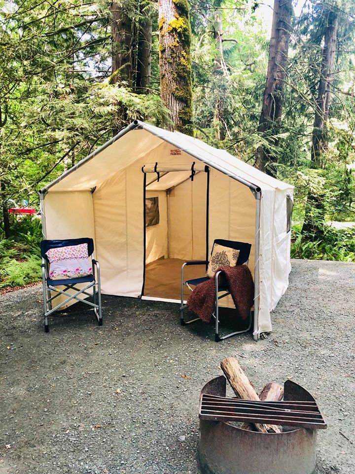 A tent is sitting next to a fire pit in the middle of a forest.