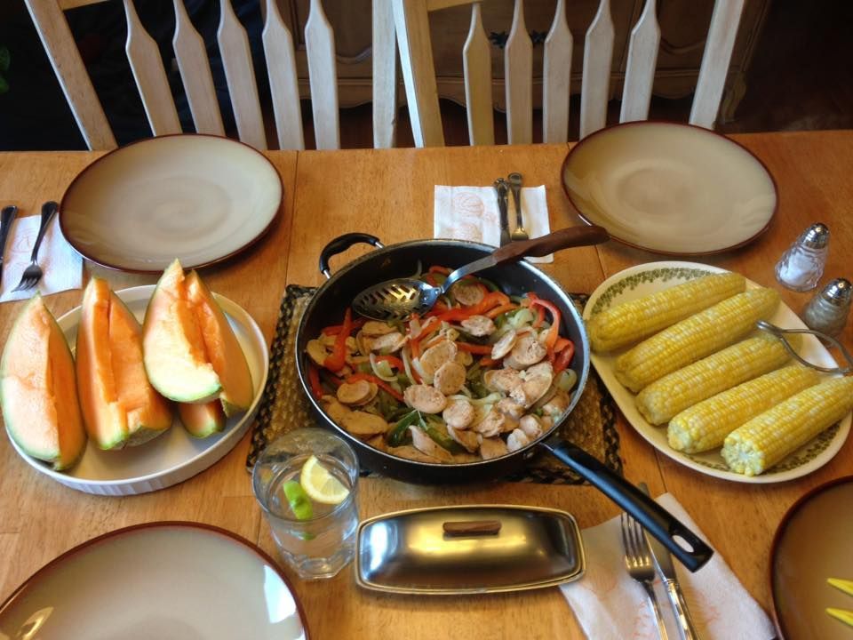 A table topped with plates of food including corn on the cob and melon
