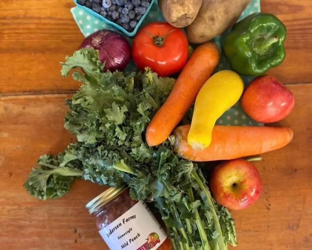 A jar of tomato sauce sits on a wooden table surrounded by fruits and vegetables.