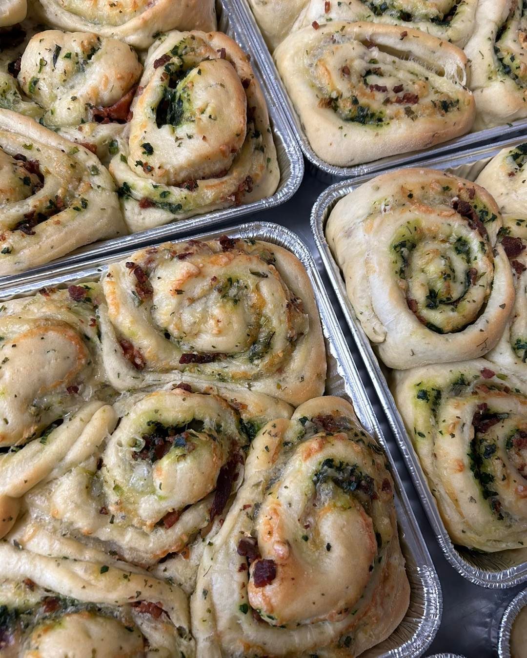 A bunch of rolls are sitting on top of each other in tin foil pans.