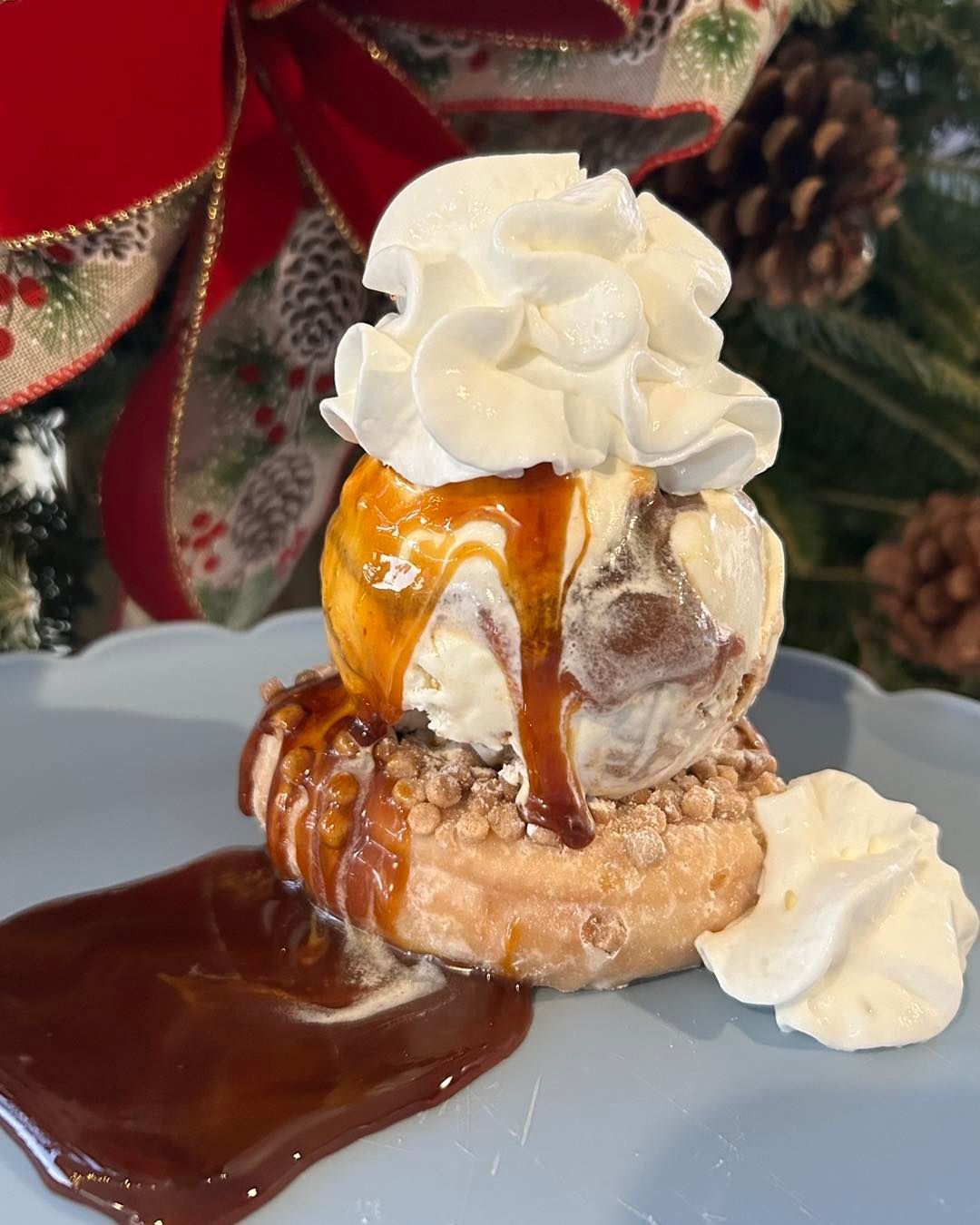 A dessert with ice cream , whipped cream , caramel sauce and chocolate sauce on a plate.