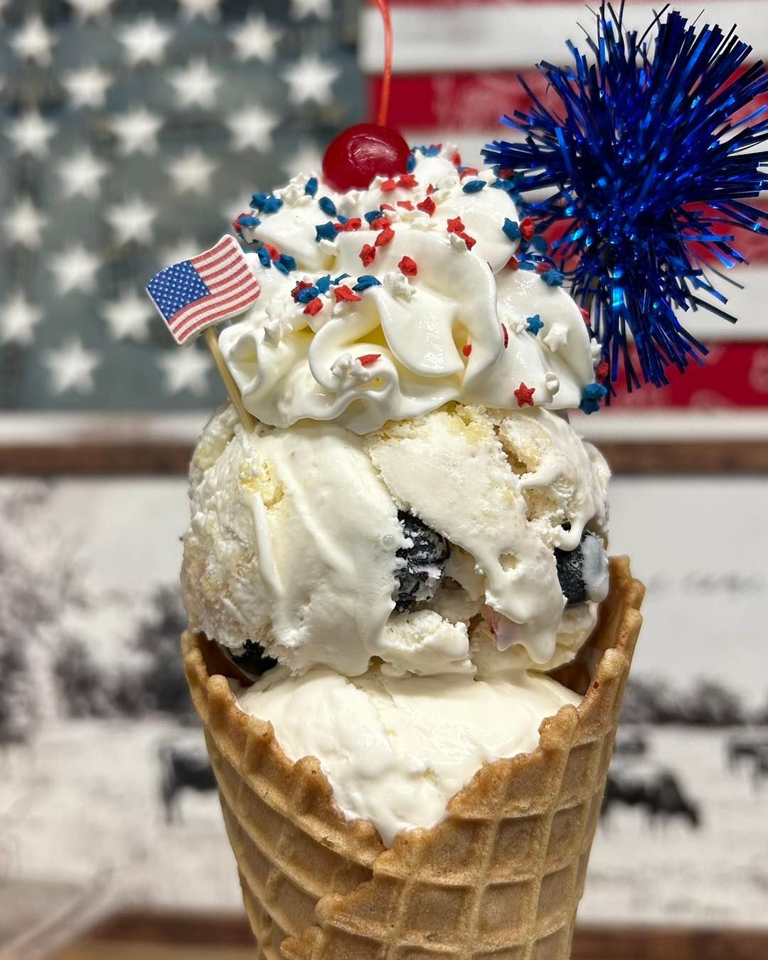 A cone of ice cream with whipped cream , sprinkles and a cherry on top.