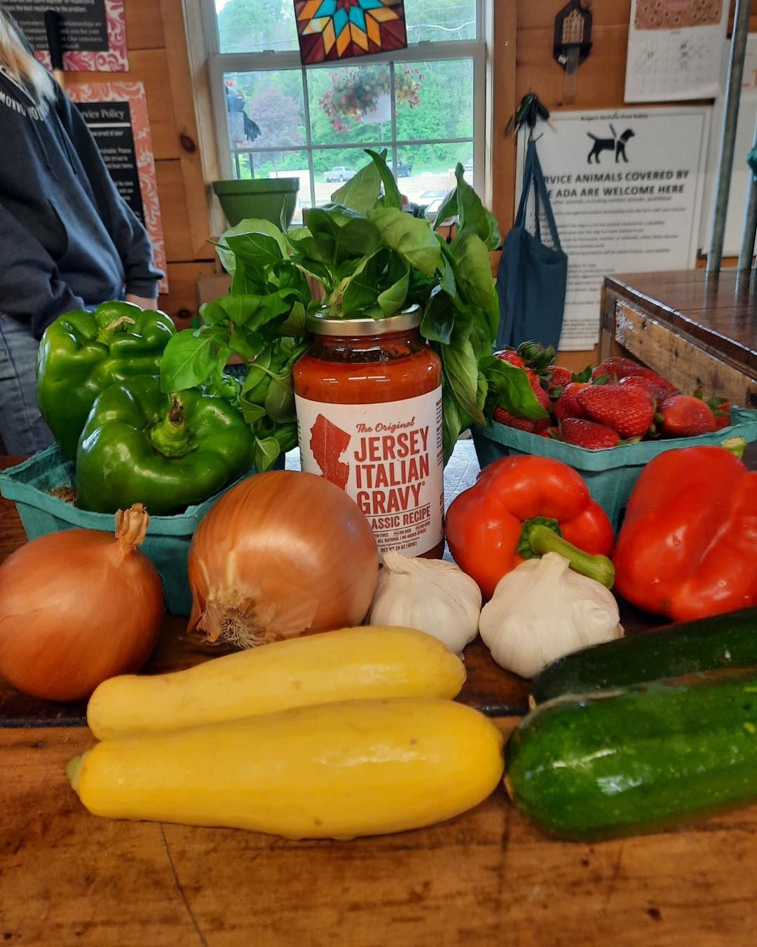 A bottle of jersey italian spaghetti sauce is surrounded by vegetables on a wooden table.