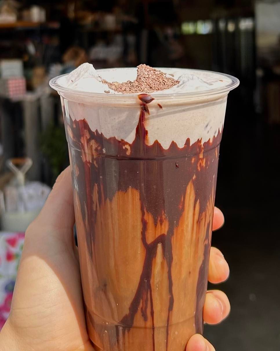A person is holding a cup of chocolate milkshake with whipped cream on top