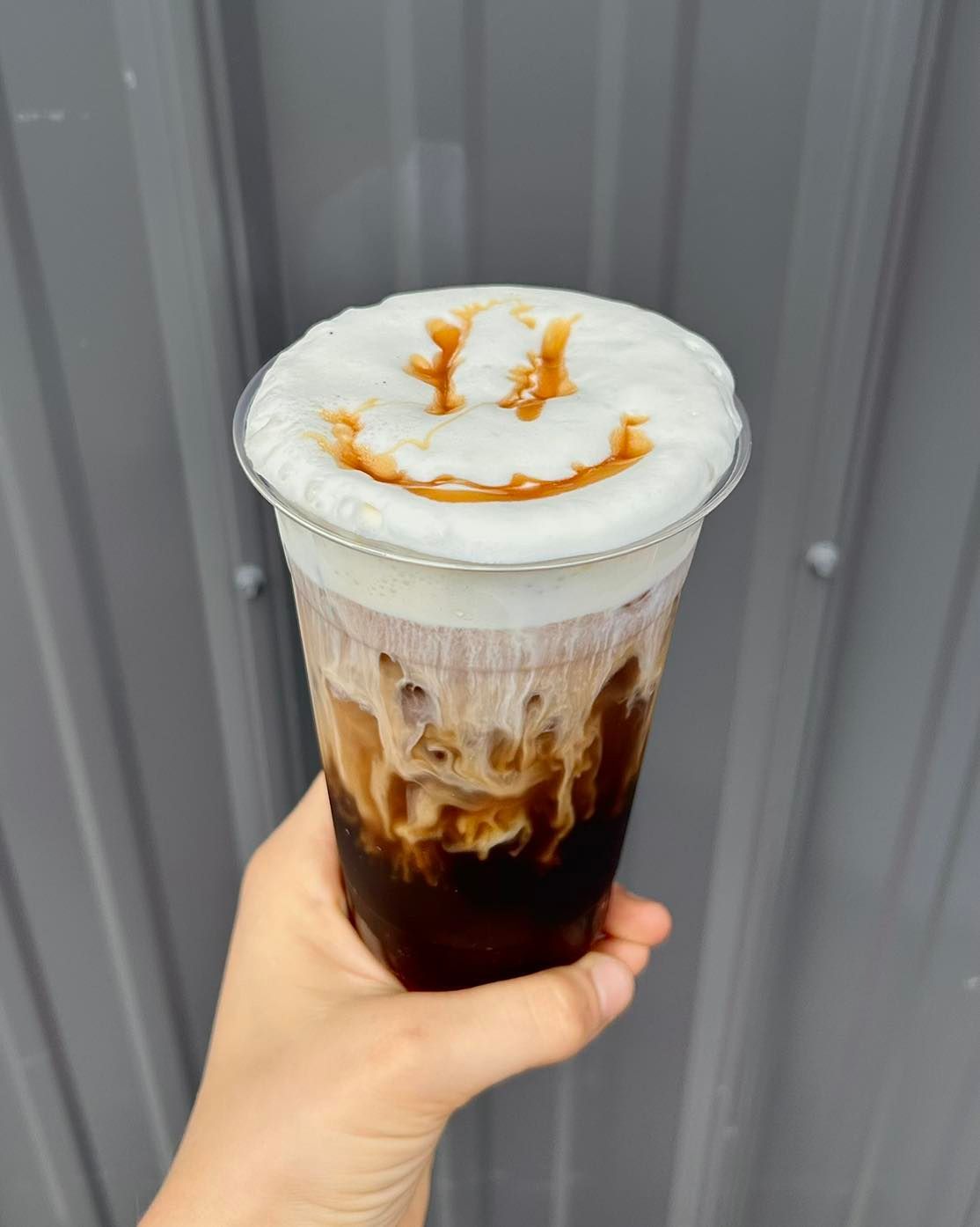 A person is holding a cup of coffee with a smiley face on top.