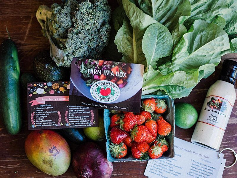 A table topped with fruits and vegetables and a box of strawberries.