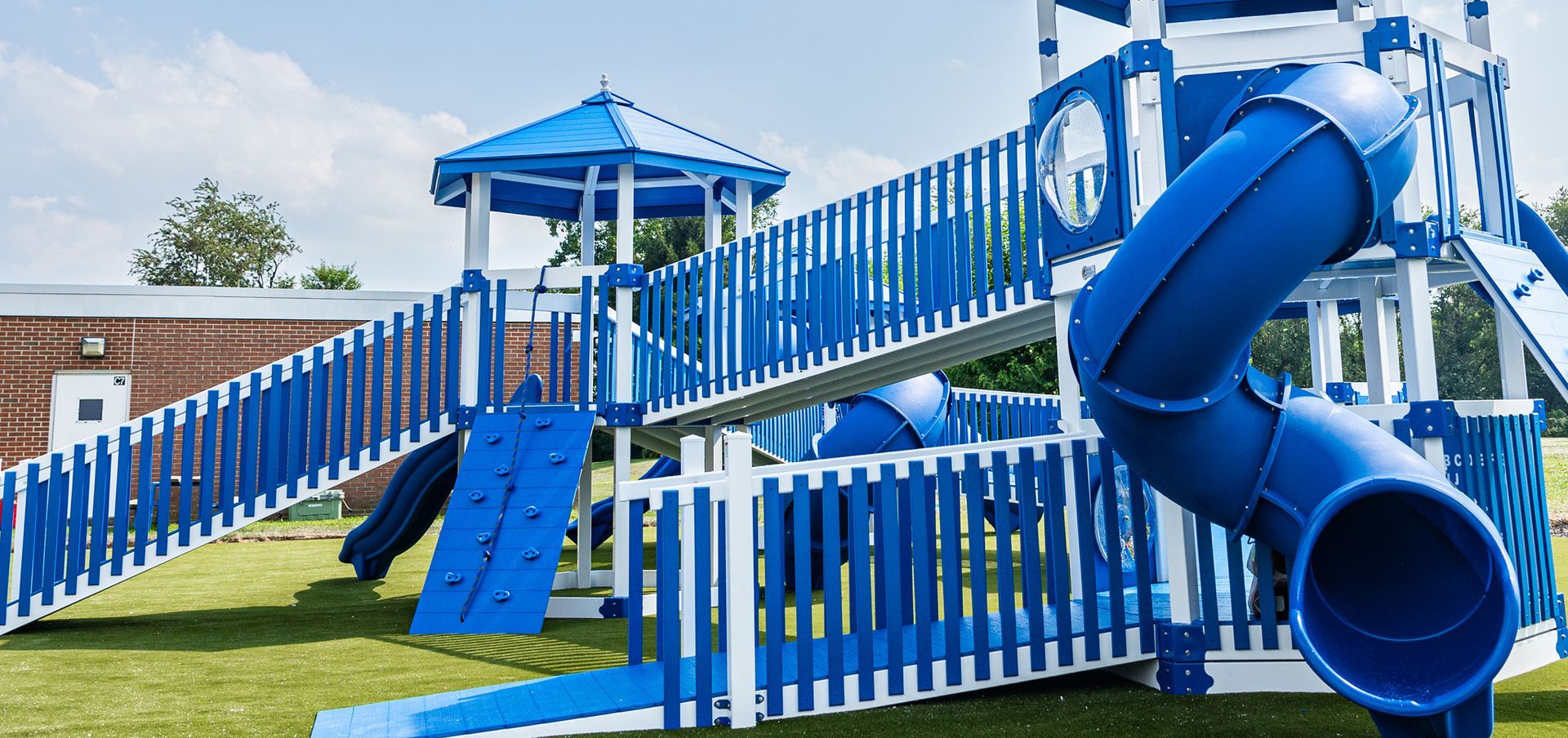 A blue and white playground set with a slide , climbing wall , and bridge.