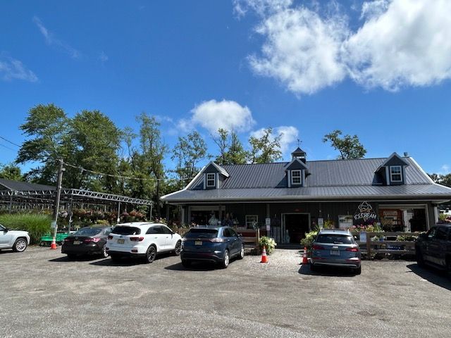 Exterior of a gray-roofed building with a small cupola, several cars parked in front. Lush greenery and blue sky.