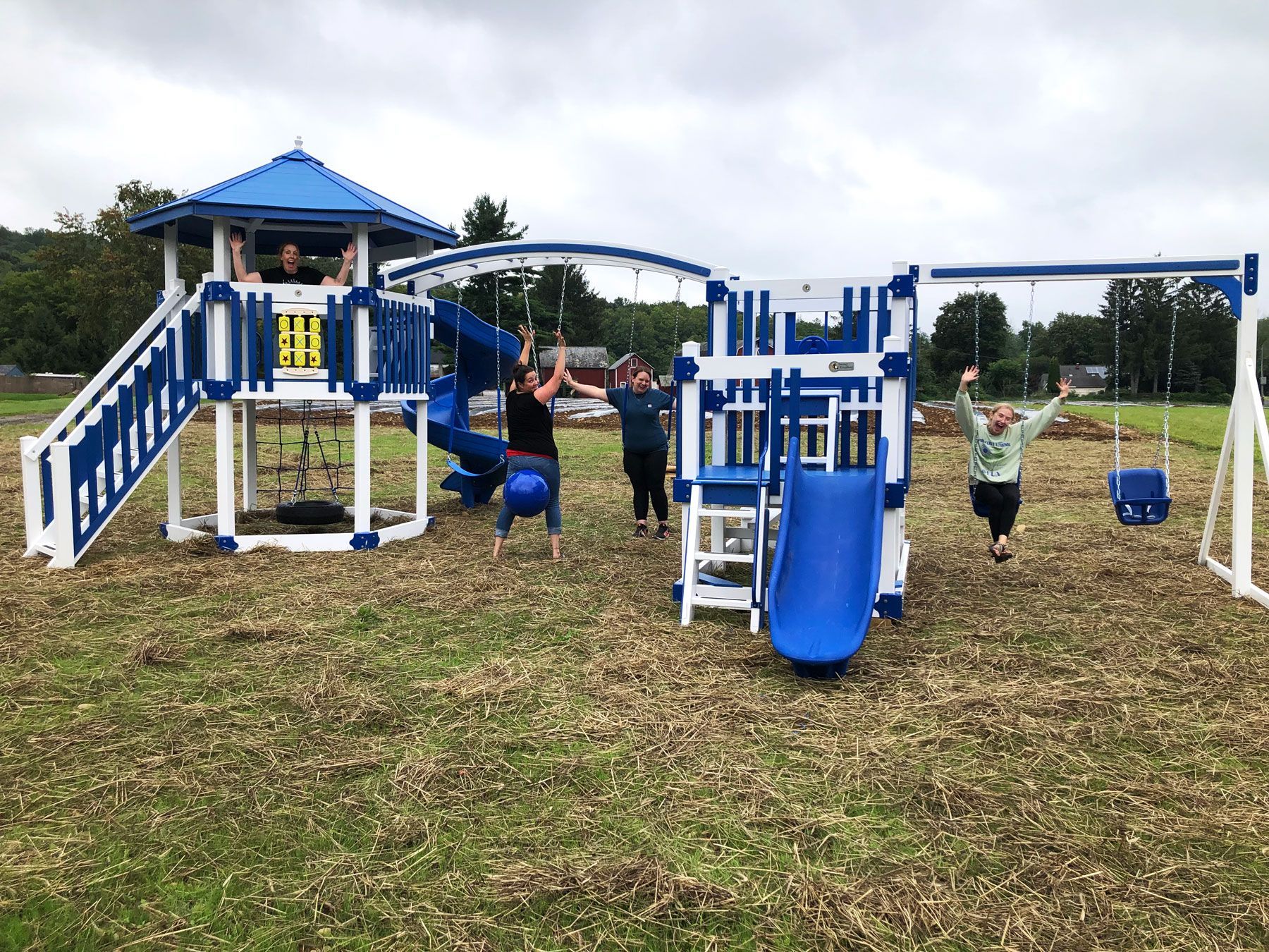 A group of people are standing in front of a blue and white playground set.