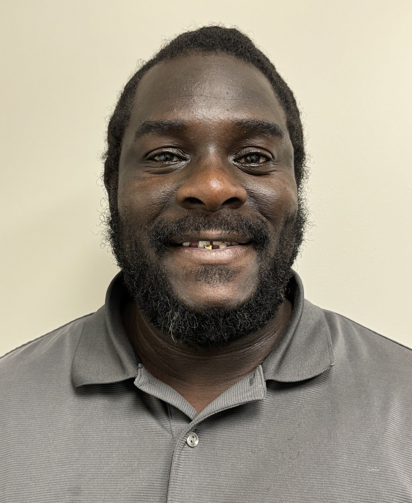 A man with a beard is smiling for the camera while wearing a grey shirt.