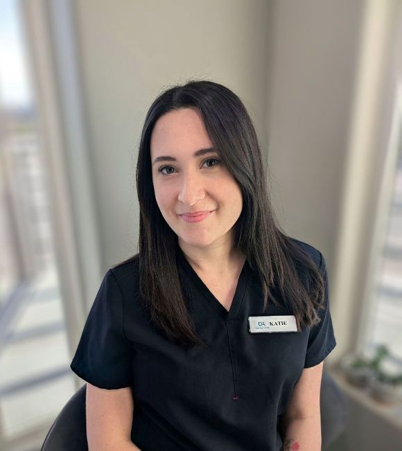A woman in a black scrub top is sitting in a chair and smiling.