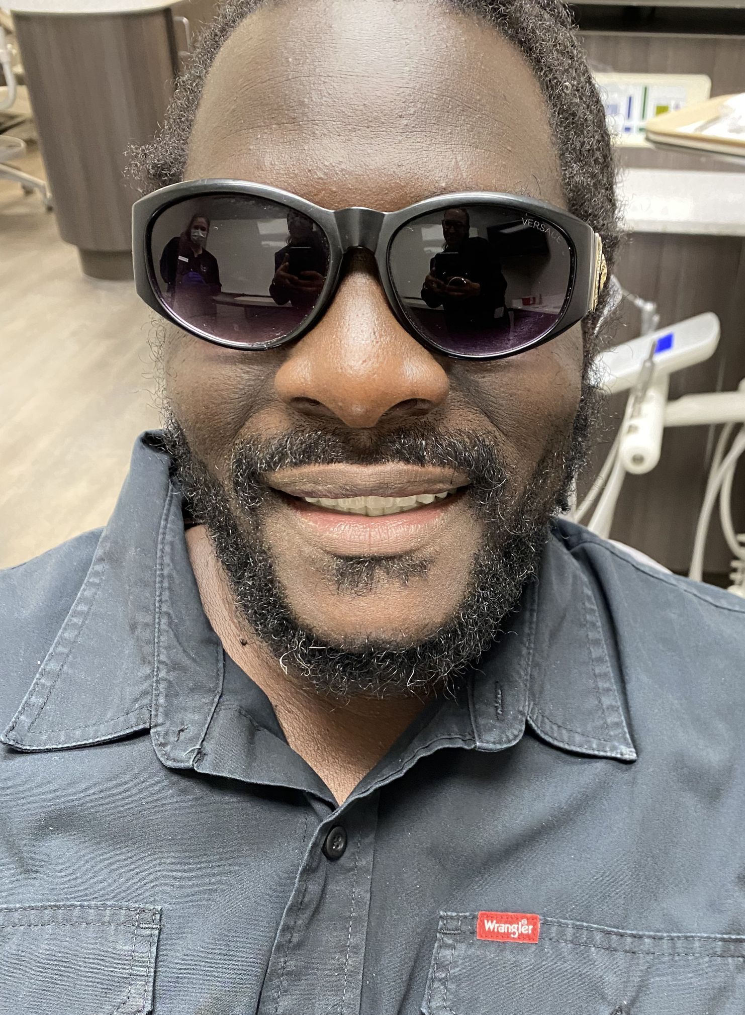 A man with a beard and sunglasses is smiling in a dental office.